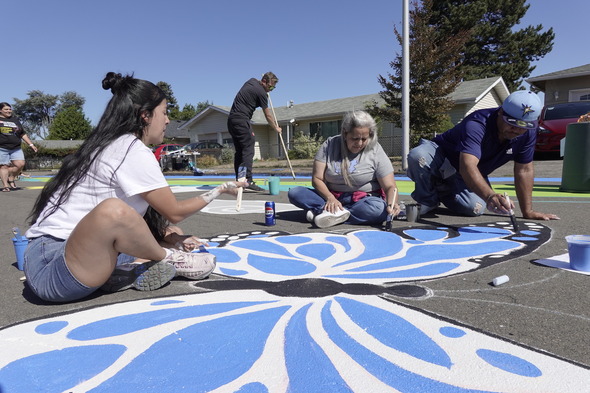 A group of people sit around to paint a large butterfly on the street.