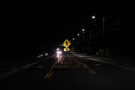 An illuminated yellow crosswalk sign in the center median of a two-way street at night. 