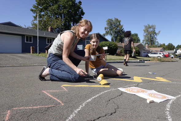 Sarah Figliozzi and her daughter smile, sitting on asphalt and painting the 131st street mural.