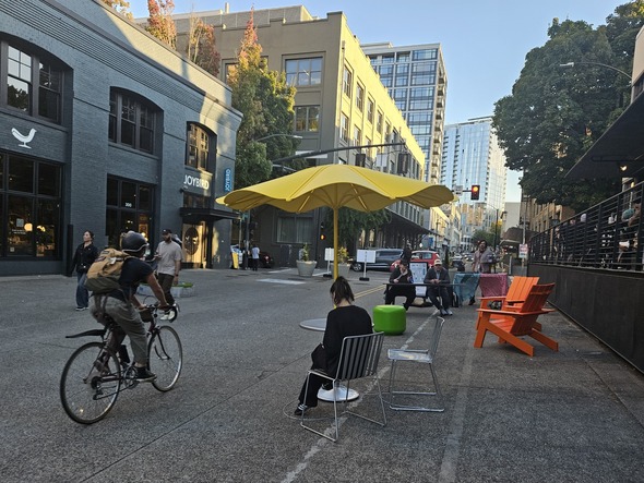 People lounge a various different pieces of furniture on NW 13th for Lounge Lab. A biker passes by.