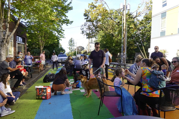 A large crowd of people gather at the colorfully painted Concordia Commons. Children get their faces painted, people walk dogs, eat, and chat.