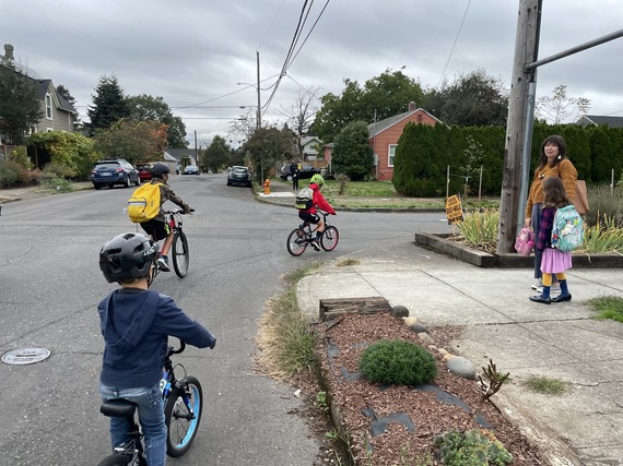 Three elementary school students on round the corner on their bikes as two pedestrians watch.