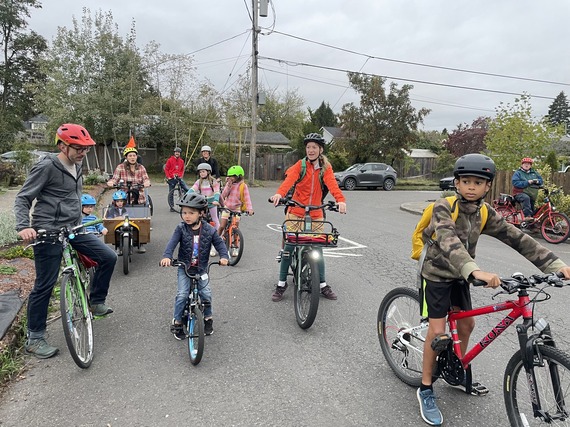 A dozen adults and elementary school students wait on a neighborhood street to start biking to school.