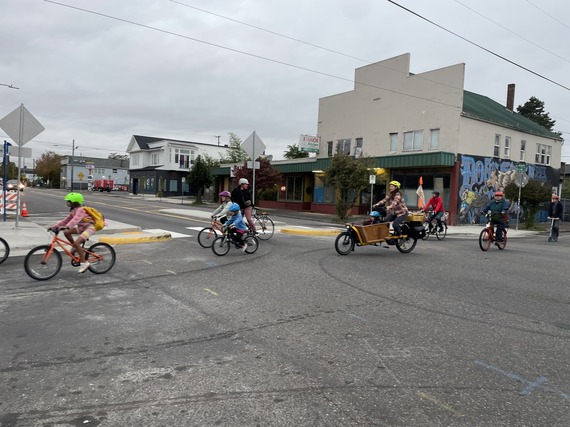 About ten adults and children ride bikes across an intersection with a new crossing median.