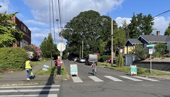 A child rides their bike on a street lined by two green "school street" signs next to a school.