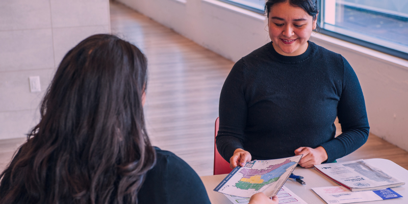 A person hands out a district map to a woman with dark hair.