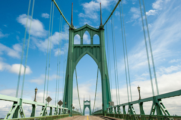 Looking up at the St. Johns Bridge towers from the deck of the bridge with white clouds and blue sky