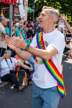 Mayor Ted Wheeler wears a rainbow sash and claps while acknowledging the crowd during the Pride Parade