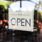Close up of a sign that reads "Welcome we're open" hanging on the glass door of a business.