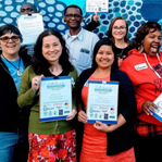A group of diverse people smile at the camera while holding certificates