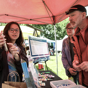 A young woman points at her phone while a couple look and listen. Brochures and flyers about the Transition are on a table.