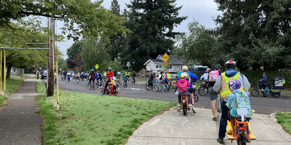 Families ride bikes along a Portland neighborhood street for Walk + Roll
