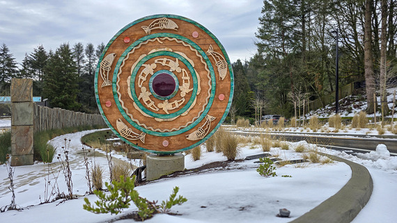 A round sculpture made of cedarwood and glass is outside in the snow at the entrance roadway to the Oregon Zoo