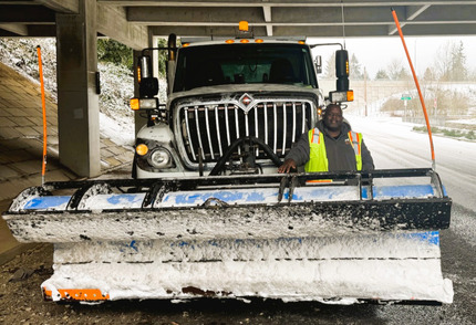 Eligeah Hodges stands in front of a snowplow on the side of the road, with the background covered in snow.