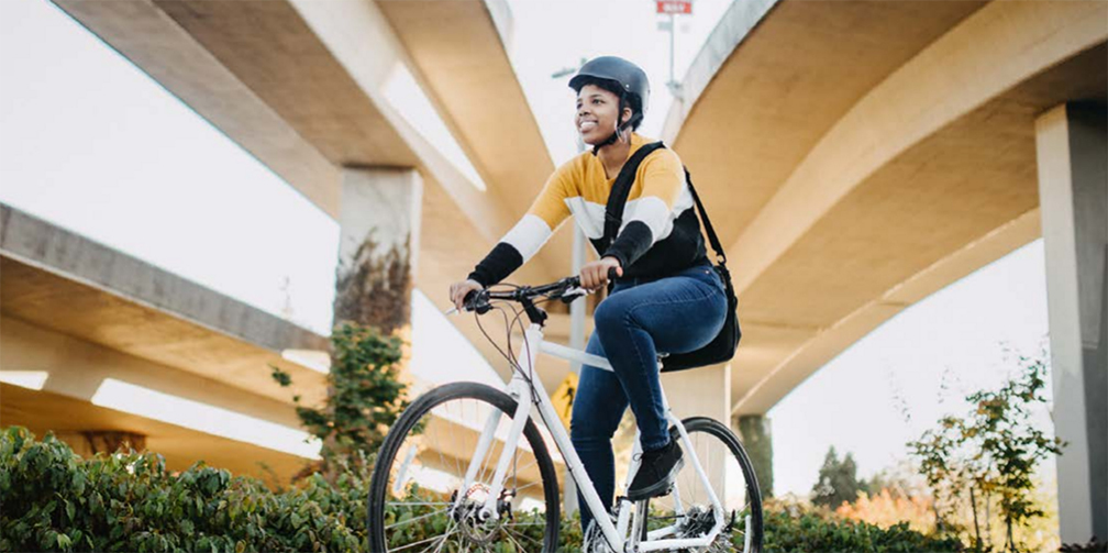 A smiling person rides a white bike on a sunny day (PBOT commute pop up)