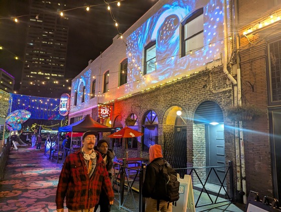 Colorful projections line the walls of Ankeny Alley while pedestrians pass through.