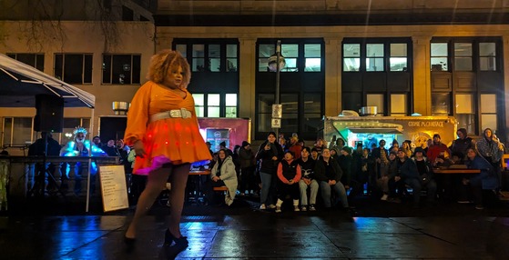 a Drag artist performs to a crowd at the cart blocks, her skirt lit with LED lights