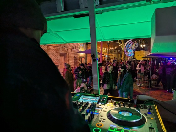 A picture from inside the Catbus shows a the back of a DJ, the crowd outside dancing, and the Nautilus sculpture in the background.