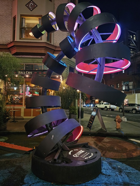 The lit up Quirk sculpture in front of Hal's Cafe at pride plaza features multiple rings lit up with glowing LED lights.