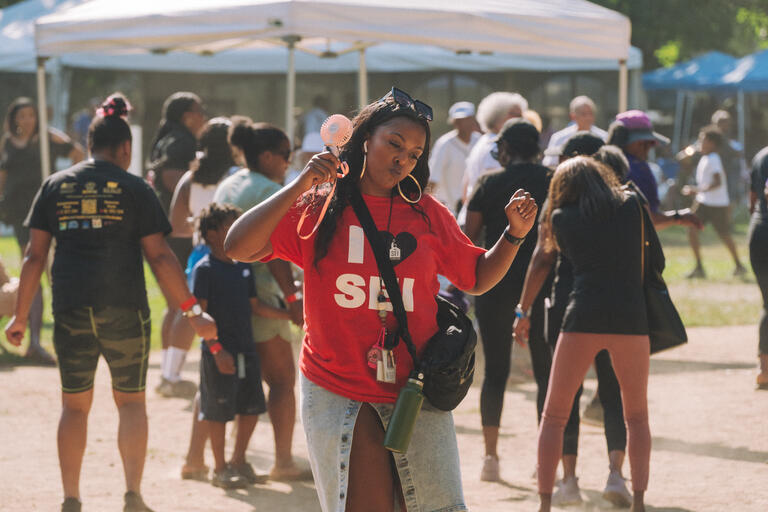 A woman with a shirt reading I heart SEI dances in the foreground of a busy community event.
