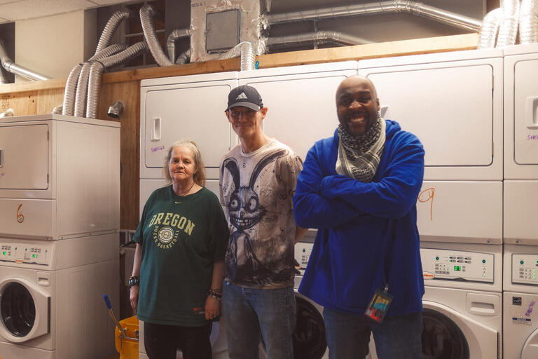 Laundry workers Annette Collins, Andrew Nelson and Terrance Freeman stand in front of washing machines at the Wash House.