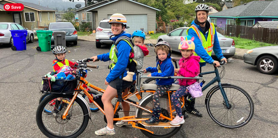 A family rides bikes together. Two parents haul four kids on an assortment of cargo bikes.