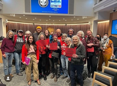 Councilor Morillo stands with advocates dressed in red in the Council chambers