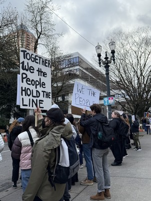 Advocates stand on the street holding signs that say "together we the people hold the line" and "we the people"