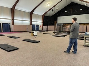 A man stands in a large room with sleeping mats 