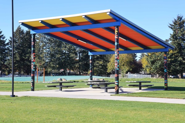 New picnic shelter with table and a bright red, yellow, and blue roof with a mural by Naomi Likayi on the columns of the shelter