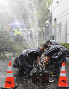 Four middle school students work on a large water pipe spewing water into the air.