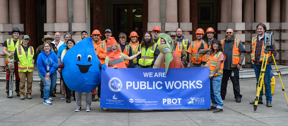 Drippy, the Water Bureau mascot that is a costume that looks like a huge drop of water, poses with Public Works staff