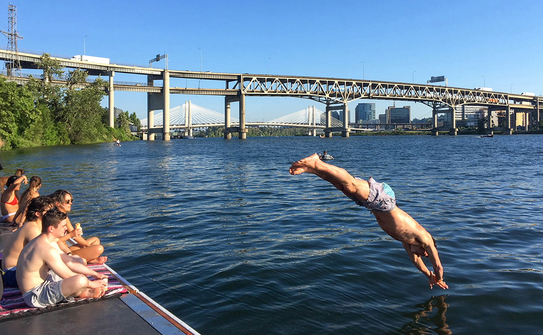 A person dives head first into the Willamette River with the Marquam Bridge in the background