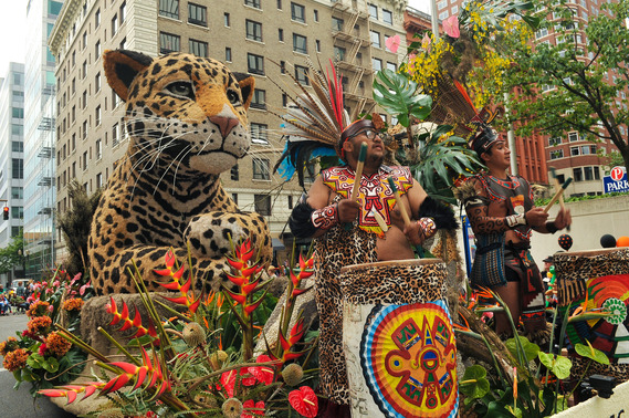 A float decorated with flowers and a large animal made of organic material with cultural performers