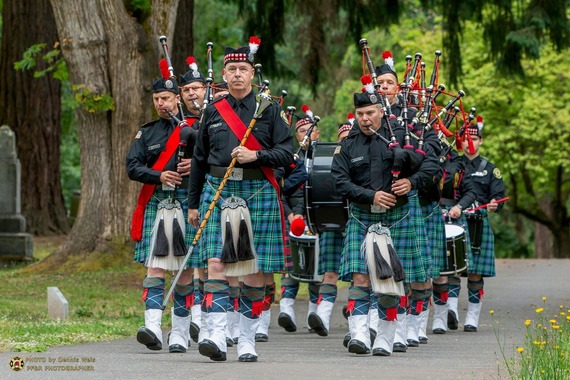 A highland band in full regalia marches in Lone Fir Cemetery playing bagpipes and drums.