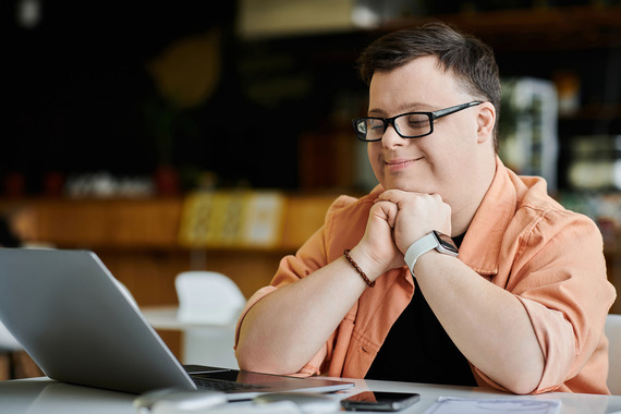 Man with Downs Syndrome smiles and works on a laptop computer - small business