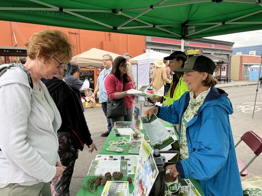 PPR- Group of people under green canopy looking at printed materials on table