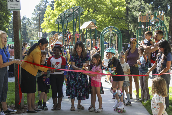 Priya Dhanapal and Tiffany Koyama Lane, along with several children, cut a ribbon to reopen Berrydale Park. The new playground is in the background.