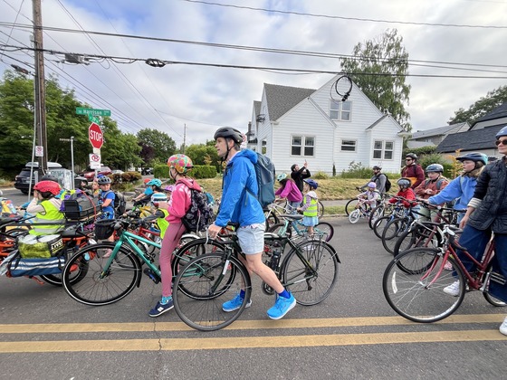 More than 15 kids and adults on bikes stop at an intersection on their way to school 