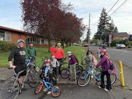 A group of eight kids and adults stand with their bikes having just arrived to school