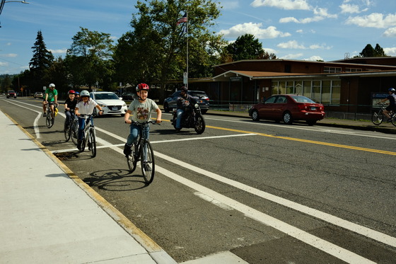 Four older elementary school students riding bikes in a bike lane as an adult teacher follows from the back.