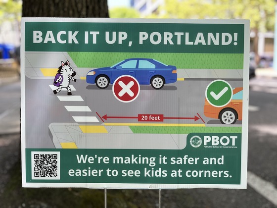 A green, horizontal yard sign titled, “Back it up, Portland!” instructs people to park cars at least 20 feet from intersections.