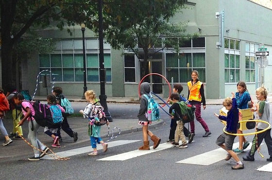 An adult crossing guard watches as 12 elementary school children walk across a crosswalk.