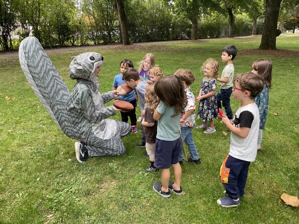 Preschool Teacher wears a squirrel costume in the park surrounded by young students learning about nature. 