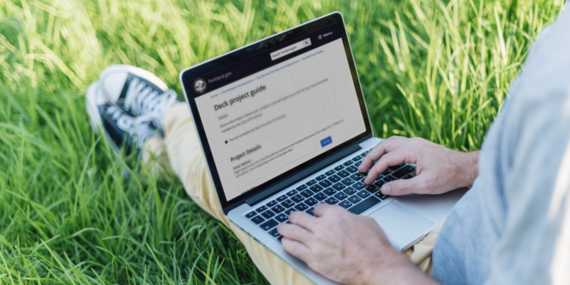 Laptop computer user sitting in grass looking at deck project guide web page