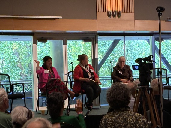 Councilor Tiffany Koyama Lane raising a hand and sitting on a panel with two other presenters on a stage at the AARP Age-Friendly Summit at PSU