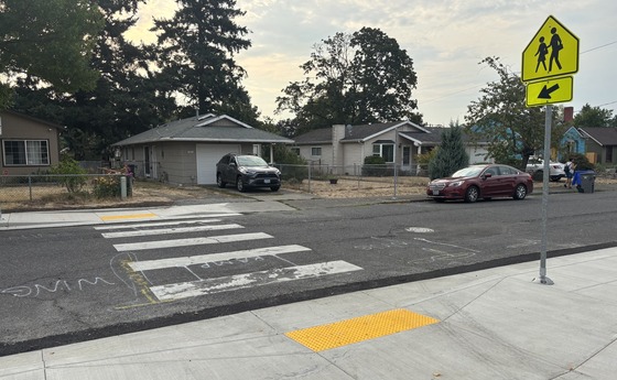 A recently improved marked crosswalk with an ADA curb ramp, a sign, and stripes.