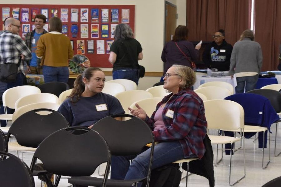 PPR - Two people seated, having a conversation in a big room with other people
