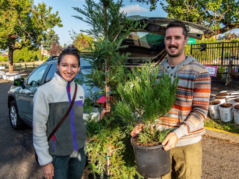 PPR - A man and woman holding small potted tree in front of a car