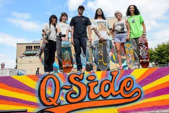 Q-Side skatepark shows six people posing with their skateboards atop a concrete barrier that's colorfully painted